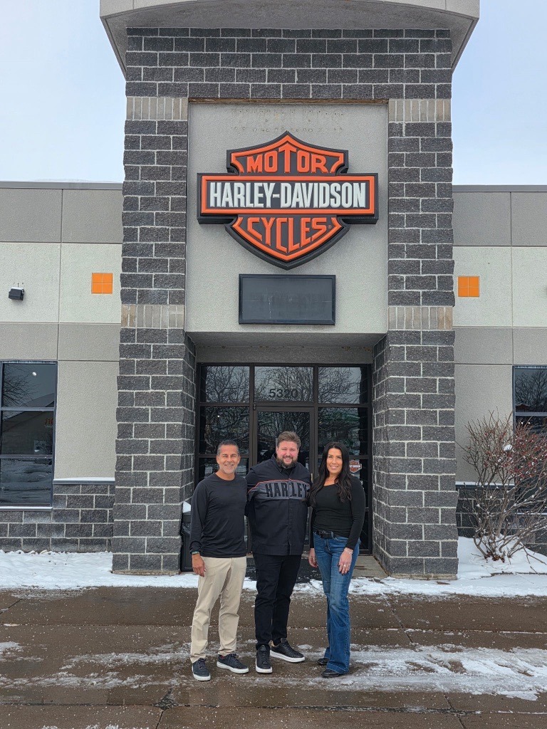 Juan Pardo, Steven Towers, and Courtney Bernhard standing in front of a Harley-Davidson dealership following a completed transaction.